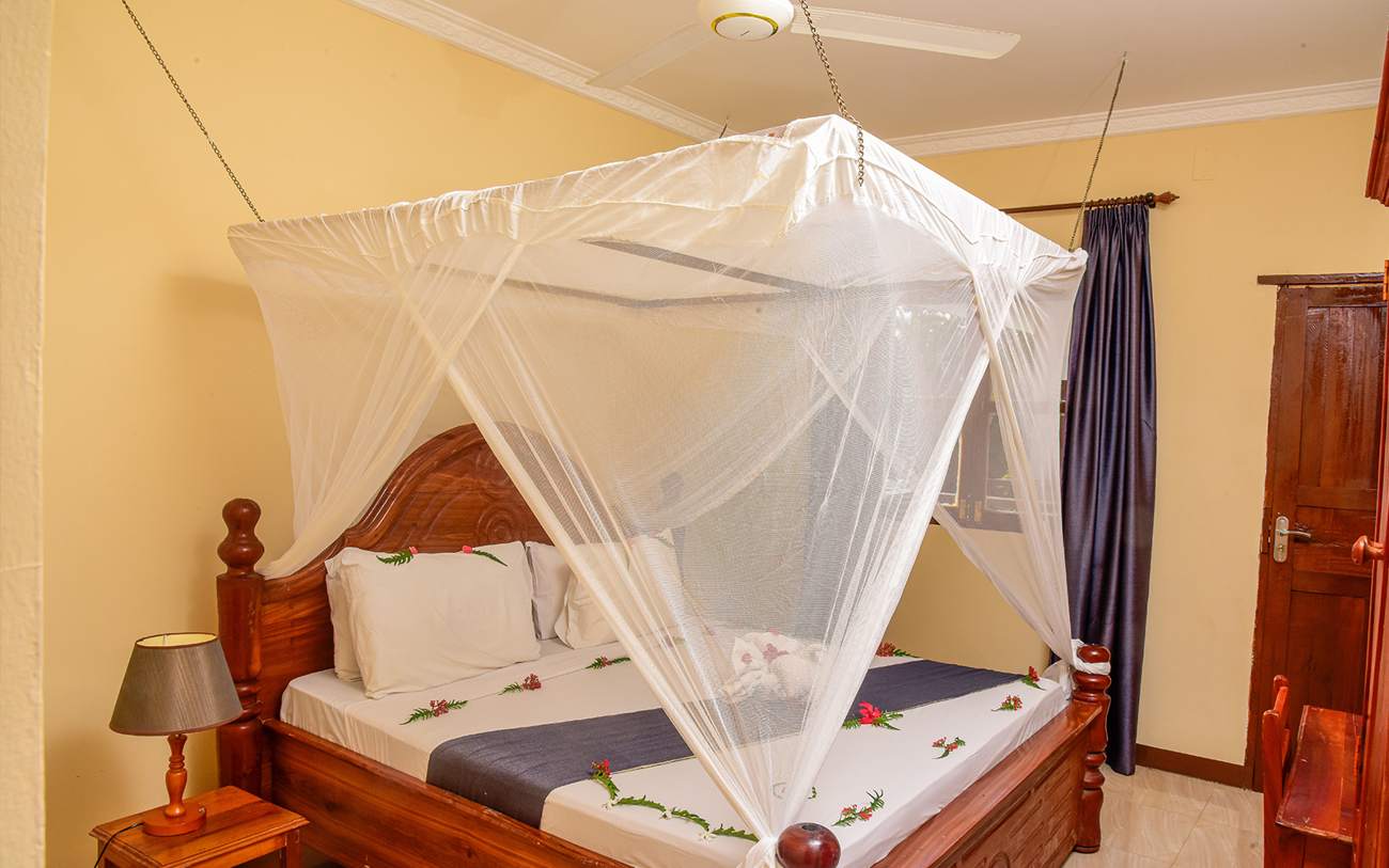 Sea-view room with carved wooden bed and mosquito net at Amaan Beach Bungalows